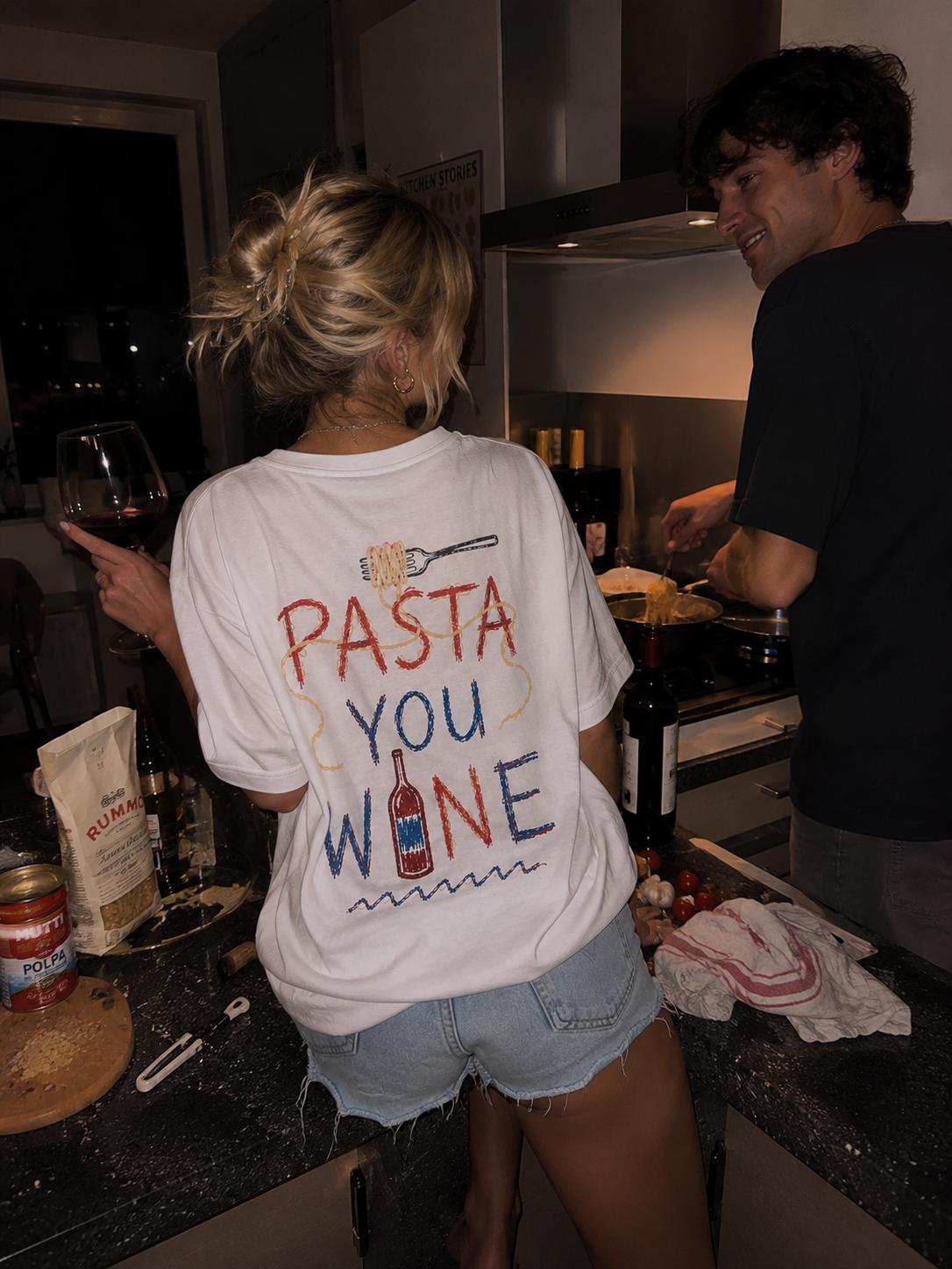Two people cooking pasta together late at night, wine in hand